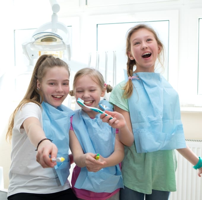 Three young girls practice tooth brushing at pediatric dentistry visit