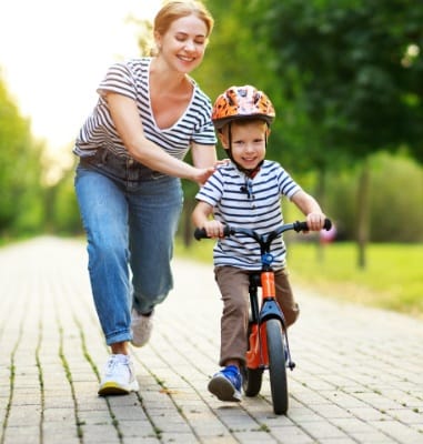 Mother helping little boy learn to ride his bike after emergency dentistry visit