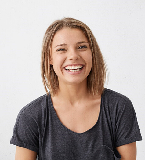 A young female wearing a gray t-shirt smiles after having a stained tooth covered with dental bonding